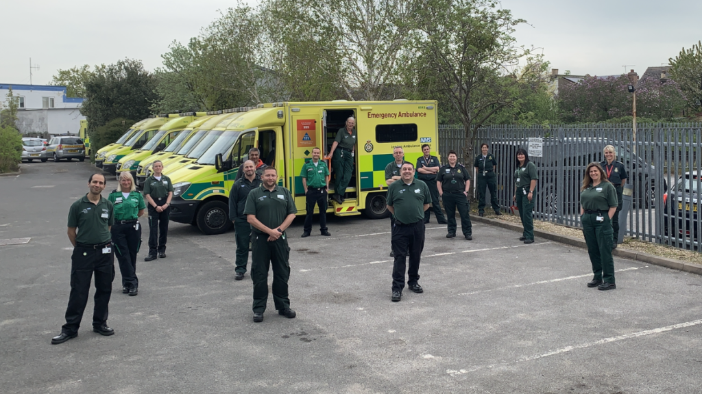 A group of London Ambulance Service trainers and St John Ambulance volunteer Community First Responders stood in front of a line of ambulances