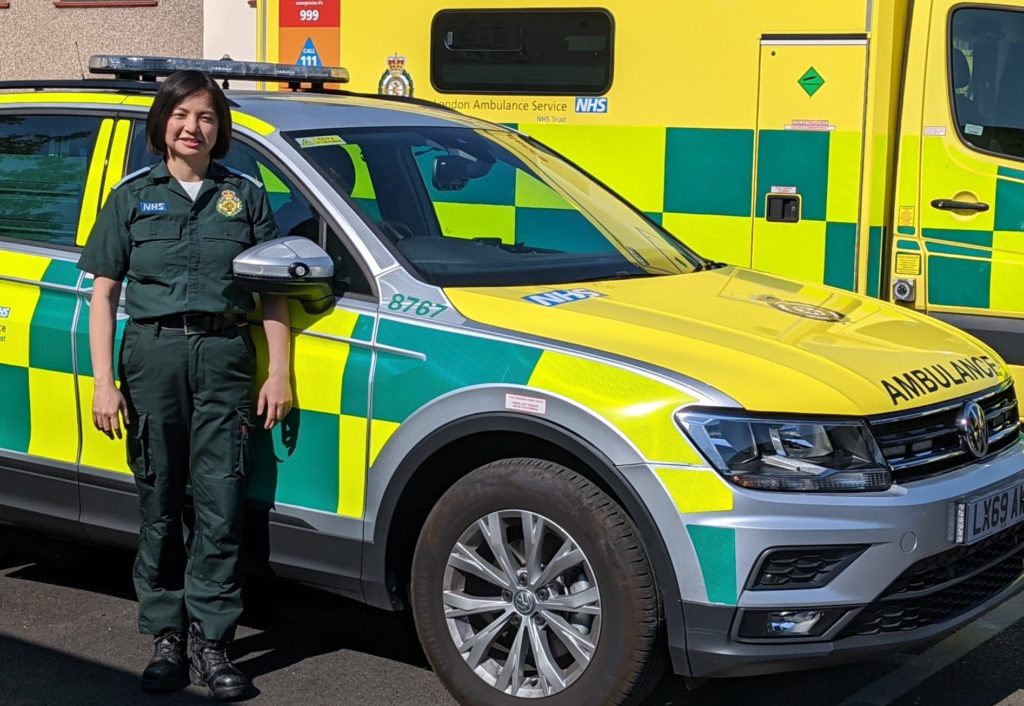 Mina stands in uniform in front of an ER response car and an ambulance