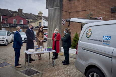 HRH The Duke and Duchess of Cambridge alongside LAS staff including Tea Truck operator Shani are shown a Tea Truck which is parked with rear door open and a table of refreshments