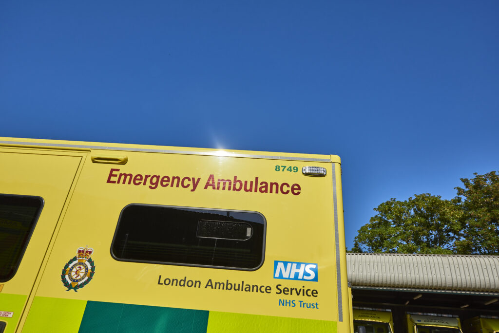 The side of an ambulance parked in an ambulance station with sunny blue sky in the background