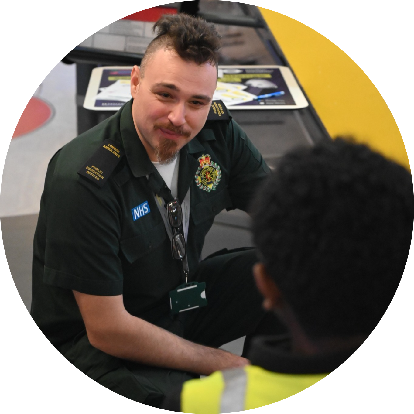 Image shows a Public Education Officer in green talking to a school pupil in a hi-vis jacket.