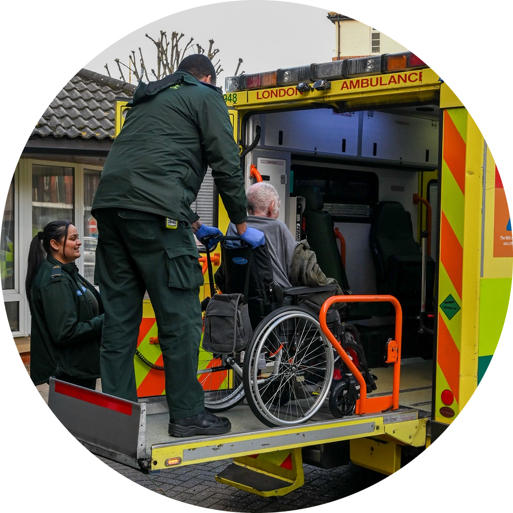 A patient in a wheelchair being tail-lifted into the back of an ambulance, supported by an ambulance crew.