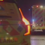 A close up of a fast-response car with an ambulance on blue lights in the background.